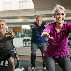 Eine Frau und zwei Männer machen gemeinsam Sportübungen in einem Fitnessraum.
