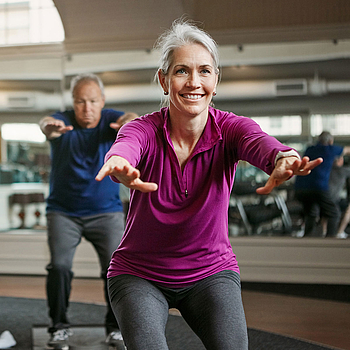 Eine Frau und zwei Männer machen gemeinsam Sportübungen in einem Fitnessraum.