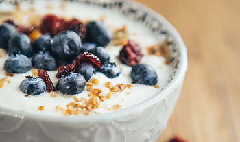 Eine weiße Schale mit Joghurt, mit Blaubeeren, getrocknete Cranberries und Nüsse als Topping.