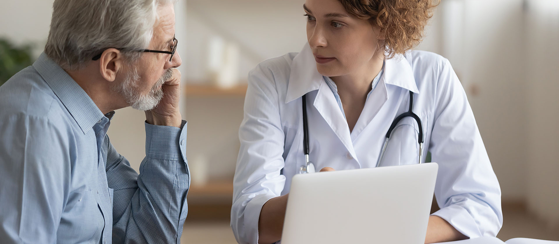 Eine Ärztin spricht mit einem älteren Patienten. Sie zeigt ihm etwas auf ihrem Laptop.