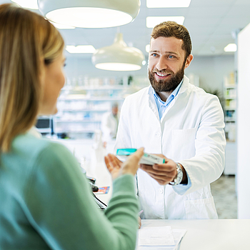 Ein Apotheker überreicht in der Apotheke einer Kundin ein Medikament.