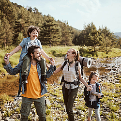 Eine Familie beim Wandern. Im Hintergrund ist Wald und ein Fluss.