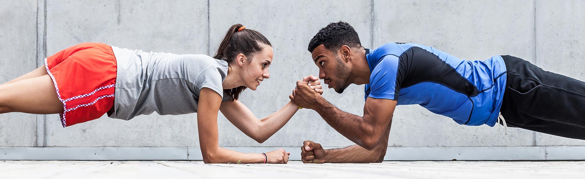 Zwei Personen halten sich im Unterarmstütz gegenüber und motivieren sich beim Training.