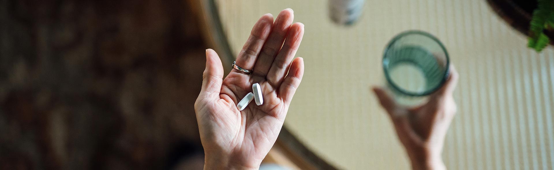 Person hält zwei Tabletten in der Hand, daneben ein Glas Wasser.