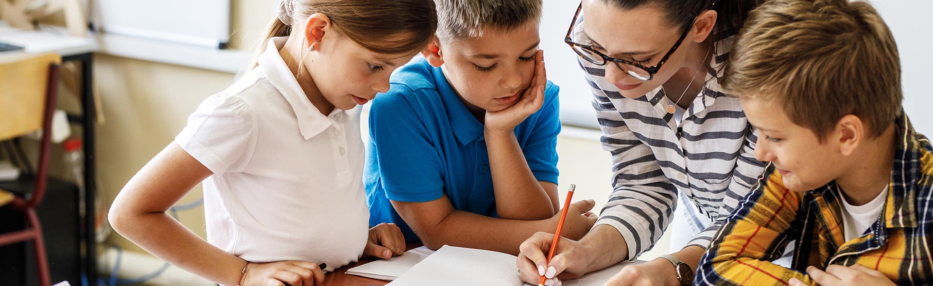 Lehrkraft unterstützt drei Kinder beim gemeinsamen Lernen am Tisch.